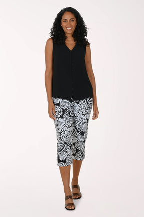 Woman wearing a black sleeveless top and patterned capri pants on a white background