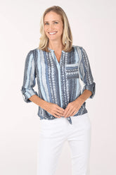 Woman wearing a blue patterned blouse and white pants on a white background