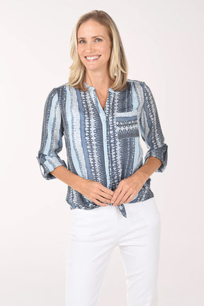 Woman wearing a blue patterned blouse and white pants on a white background