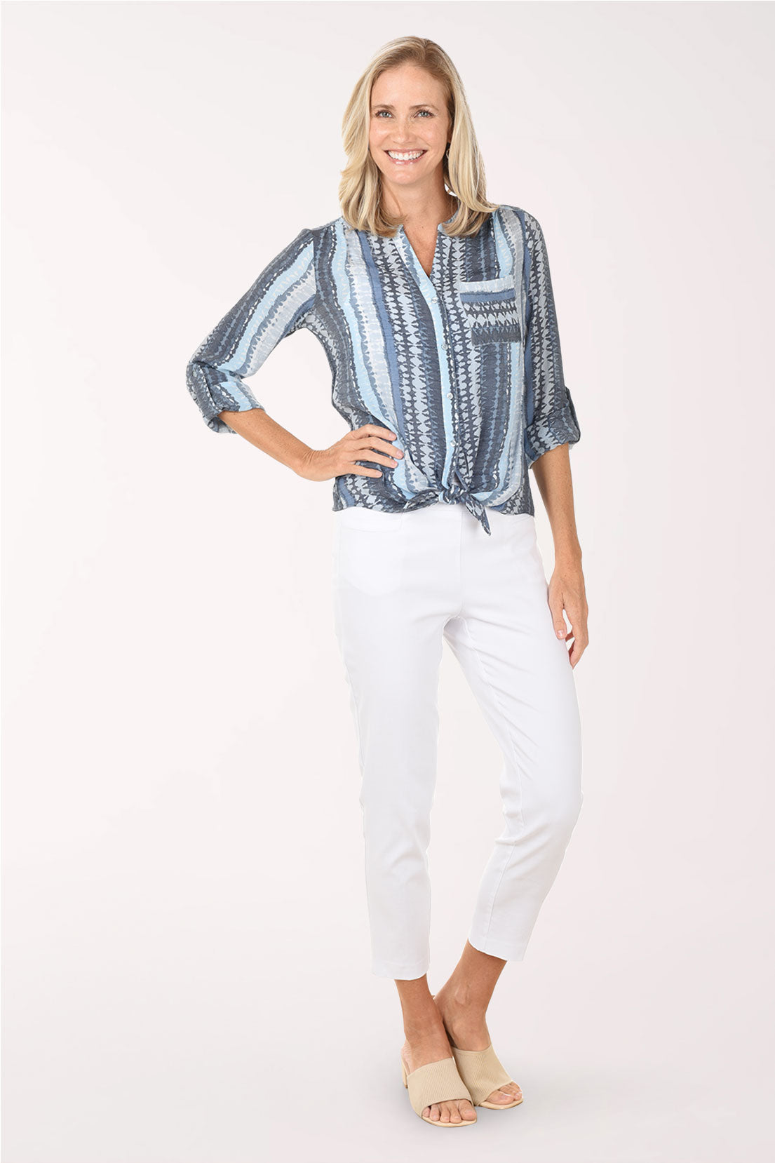 Woman wearing a blue patterned blouse and white pants on a white background