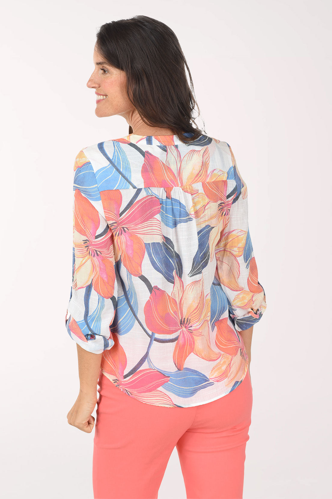 Woman wearing a colorful floral blouse and coral pants on a white background