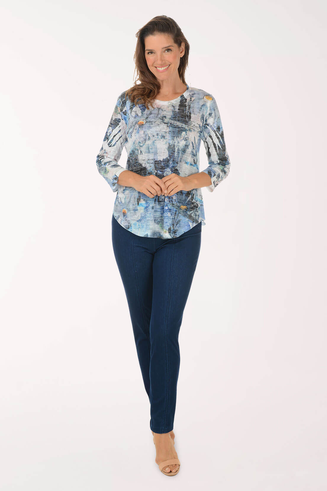 A woman wearing dark wash slim leg pull-on jeans with a blue and white abstract print 3/4 sleeve top and nude heeled sandals, shown full length.