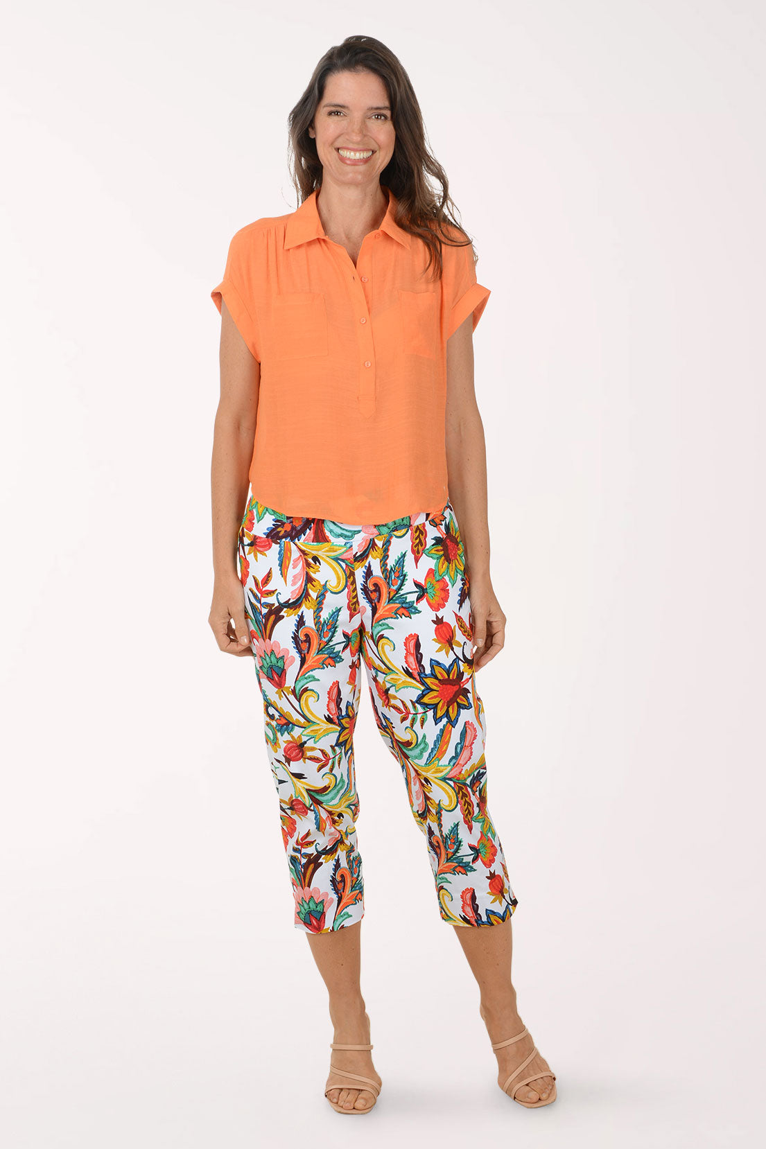 Woman wearing an orange top and colorful patterned pants on a white background