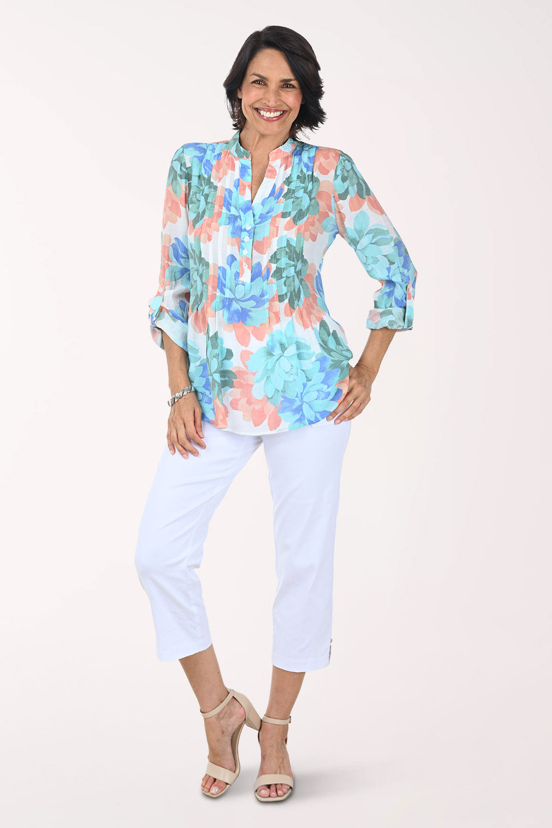 Woman wearing a colorful floral blouse and white pants on a white background