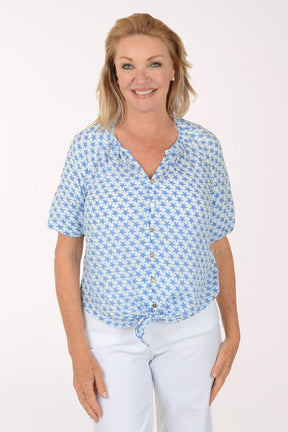 Woman wearing a blue patterned blouse and white pants on a white background
