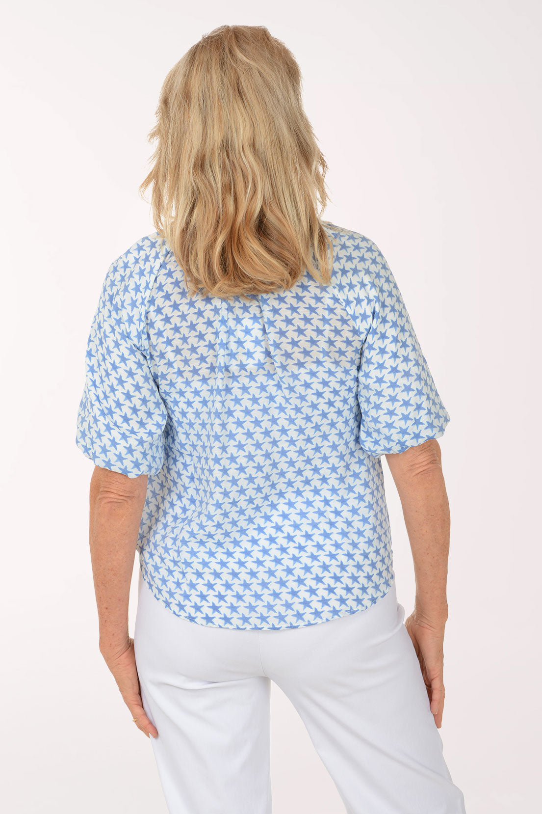 Woman wearing a blue patterned blouse and white pants on a white background