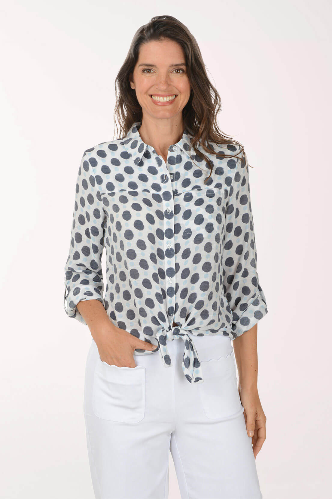 Woman wearing a patterned shirt and white pants on a plain background