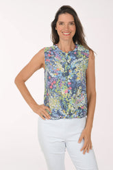 Woman wearing a sleeveless floral top and white pants on a white background