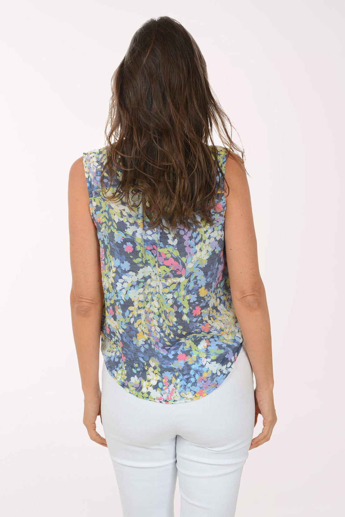 Woman wearing a sleeveless floral top and white pants on a white background