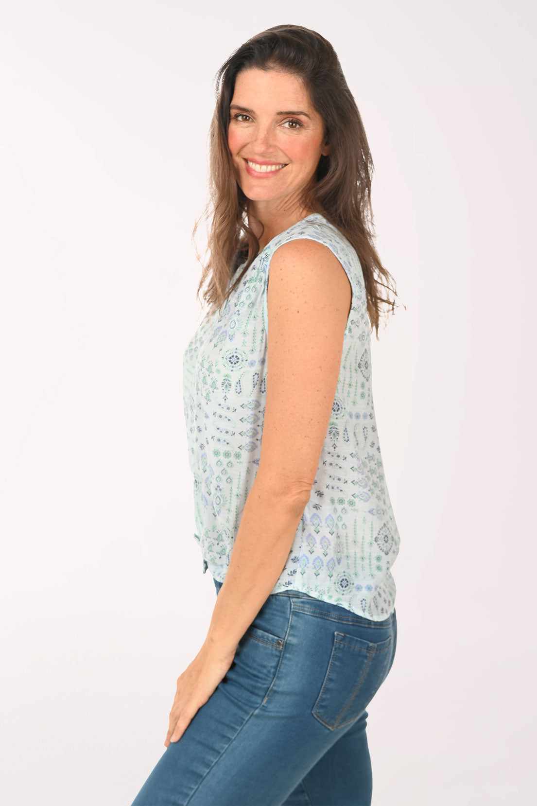 Woman wearing a light blue sleeveless top with a pattern and blue jeans on a white background