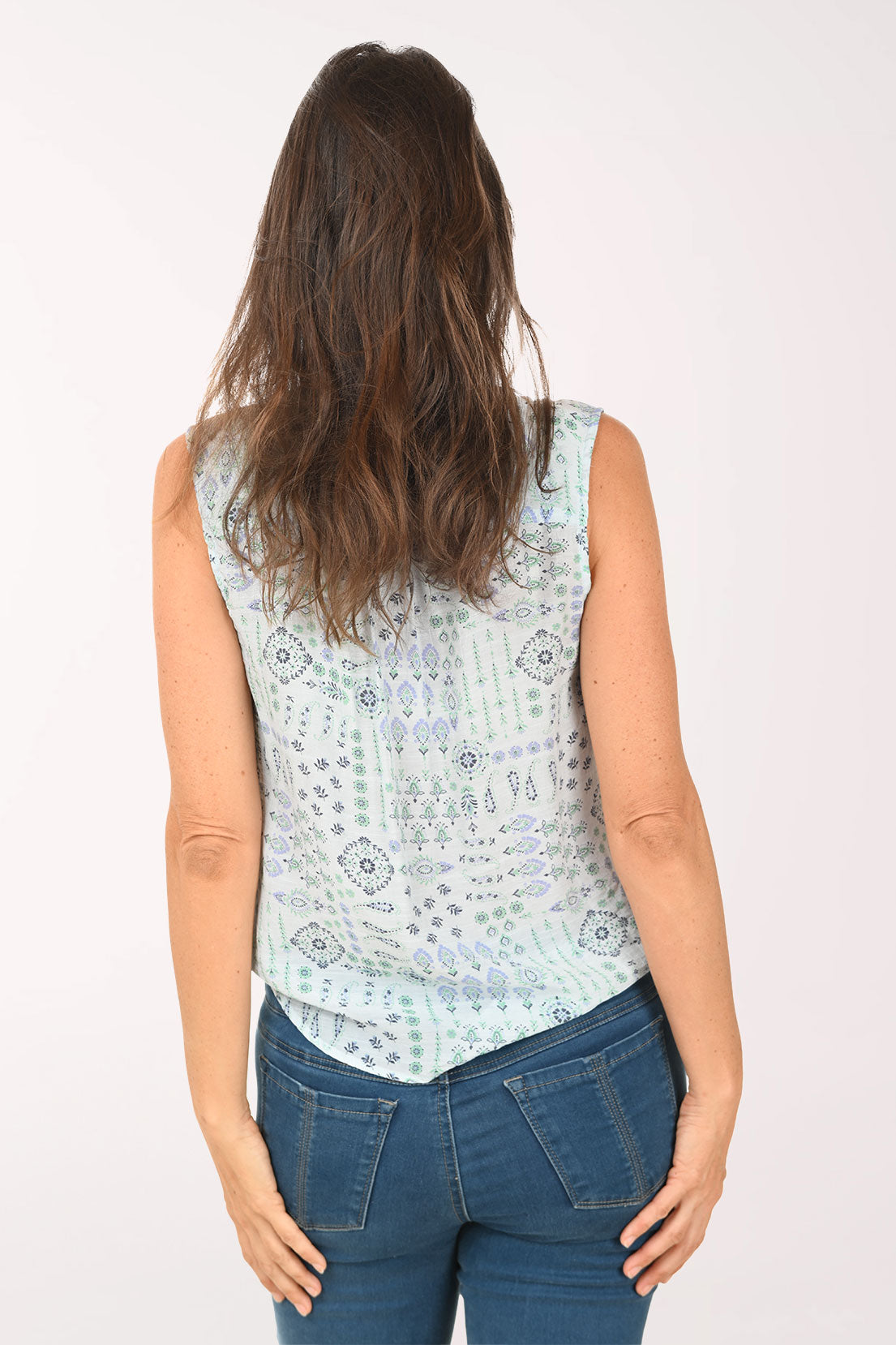 Woman wearing a light blue sleeveless top with a pattern and blue jeans on a white background