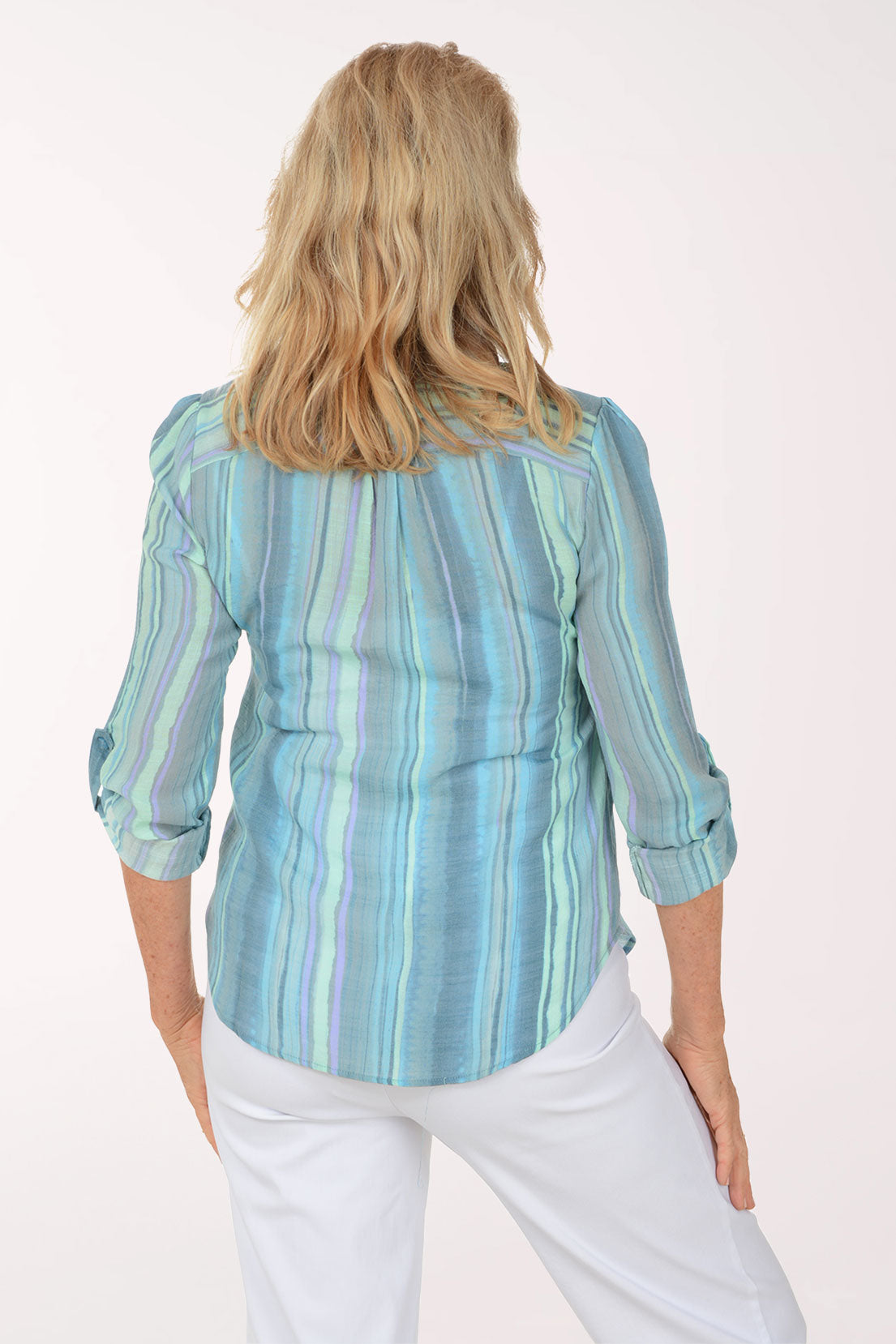 Woman wearing a light blue striped shirt and white pants on a white background