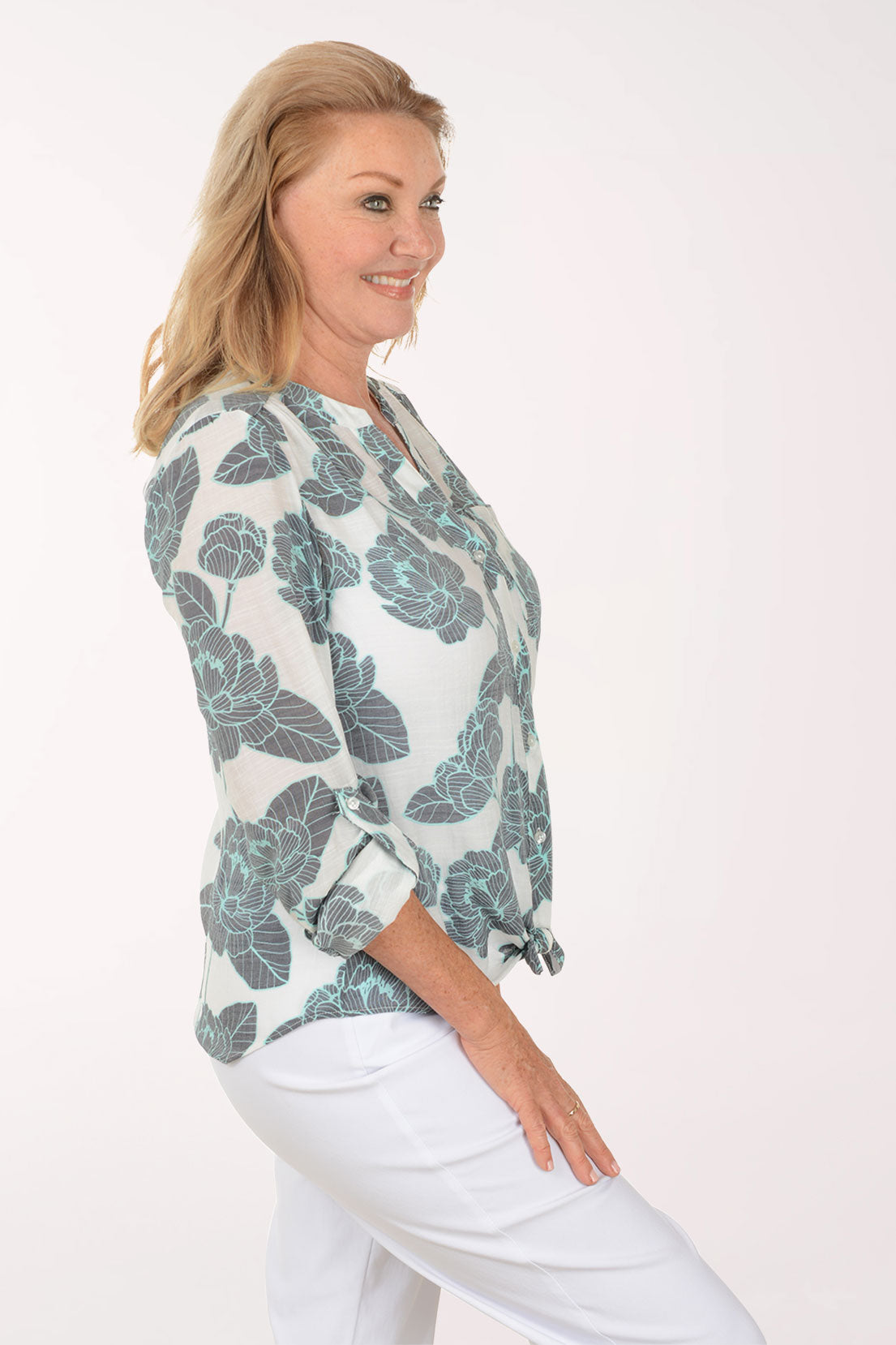Woman wearing a floral blouse and white pants on a plain background