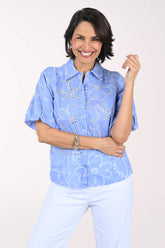 Woman wearing a blue floral blouse and white pants on a light background