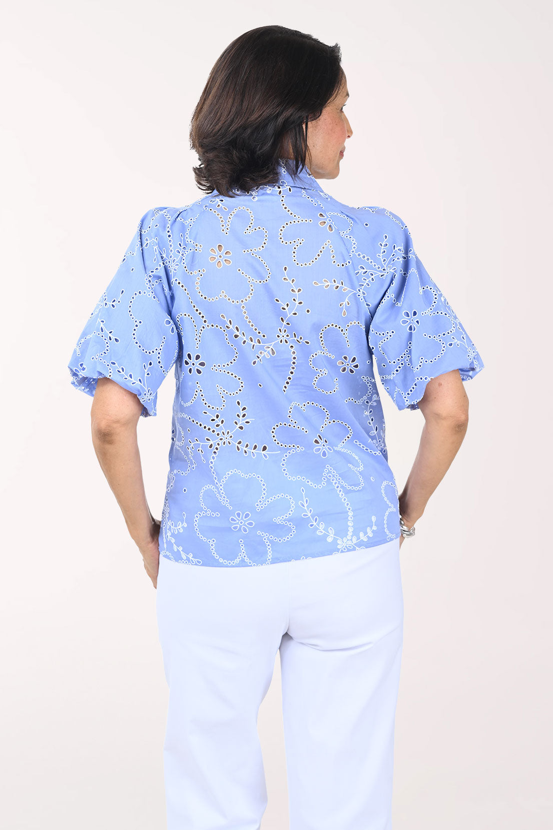Woman wearing a blue floral blouse and white pants on a light background