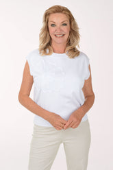 Woman wearing a white sleeveless sweater and light-colored pants on a plain background