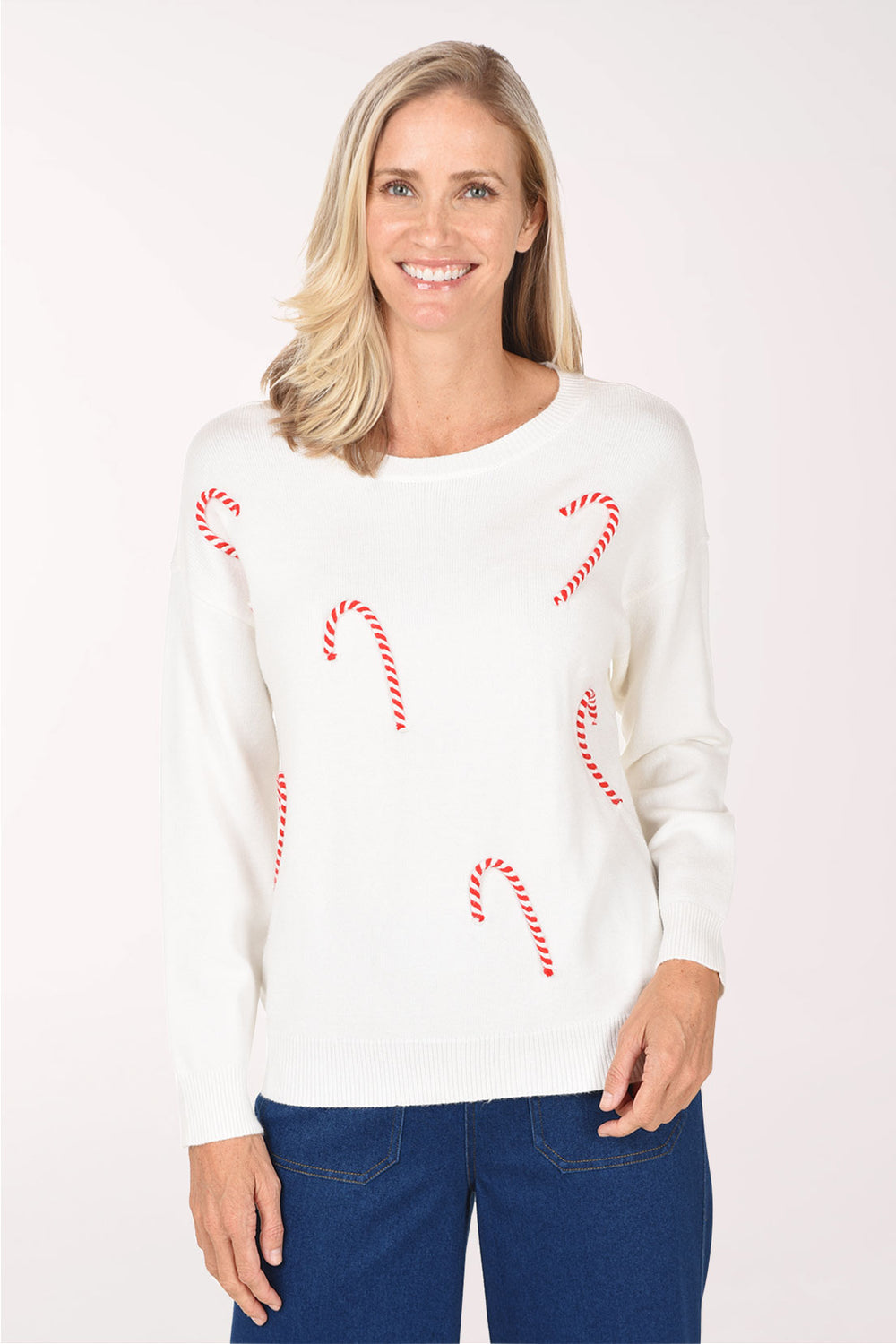 Model wearing the Zac and Rachel Candy Cane Sweater, an ivory crewneck knit with red and white embellished candy canes scattered across the front, with dark blue jeans