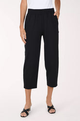 A model wearing black cropped activewear pant, paired with a white top and black sandals, against a plain light background.