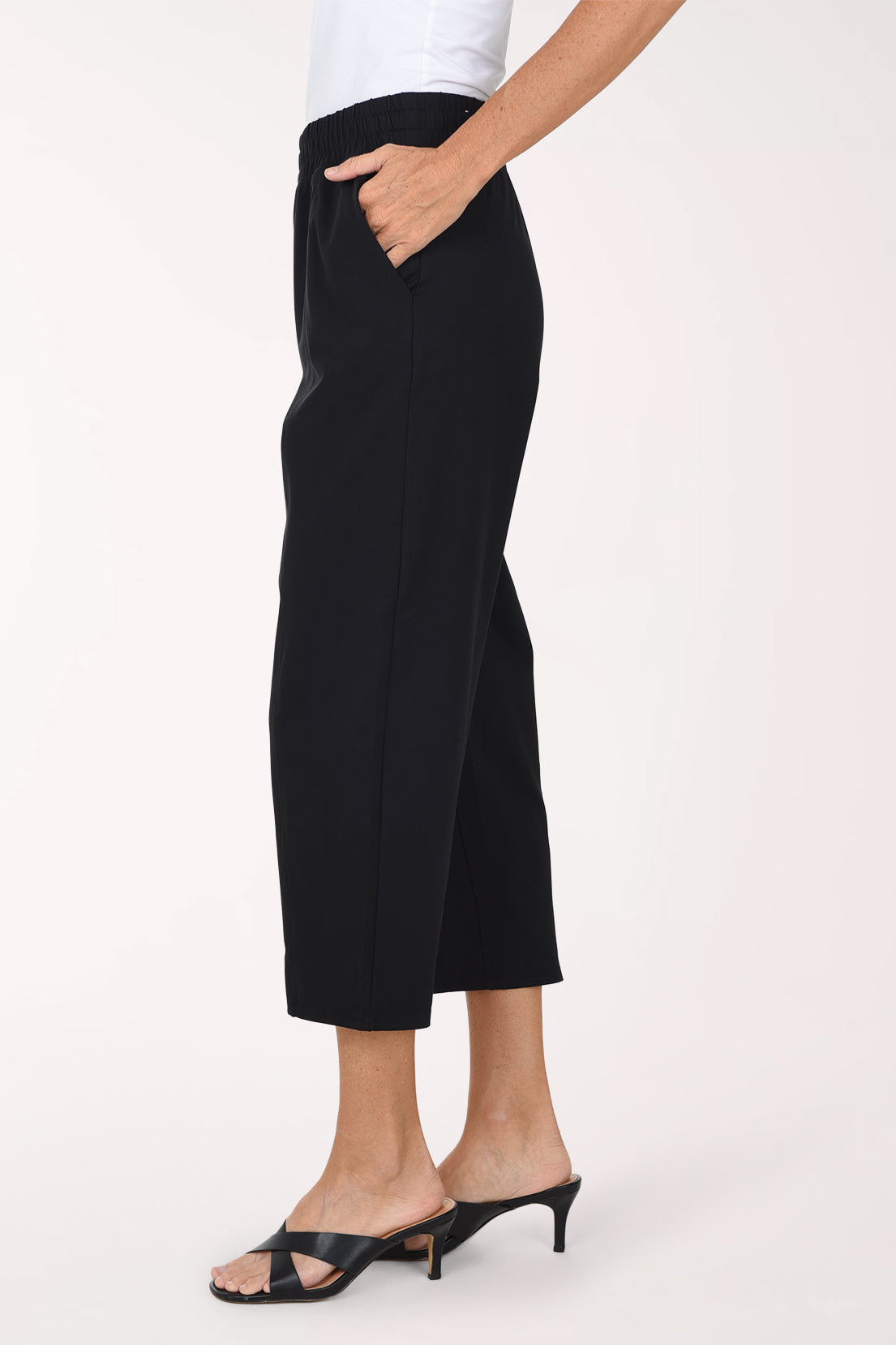 A model wearing black cropped activewear pant, paired with a white top and black sandals, against a plain light background.