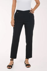 A model wearing black textured straight-leg trousers with gold-tone button details, paired with a white top and black sandals, shown from the waist down on a white studio background.