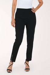 A model wearing black slim-fit ankle-length pants with decorative silver buttons on the lower hem, paired with a white top and black strappy heels, against a plain white studio background.