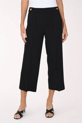 A model wearing black cropped wide-leg trousers with gold button details at the waistband, paired with a white top and black sandals, against a plain light background.