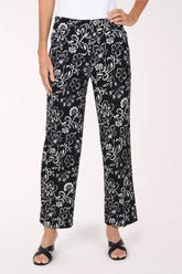 A person wearing black wide-leg cropped pants with a white floral print, paired with a white top and black slide sandals, shown against a plain light background.