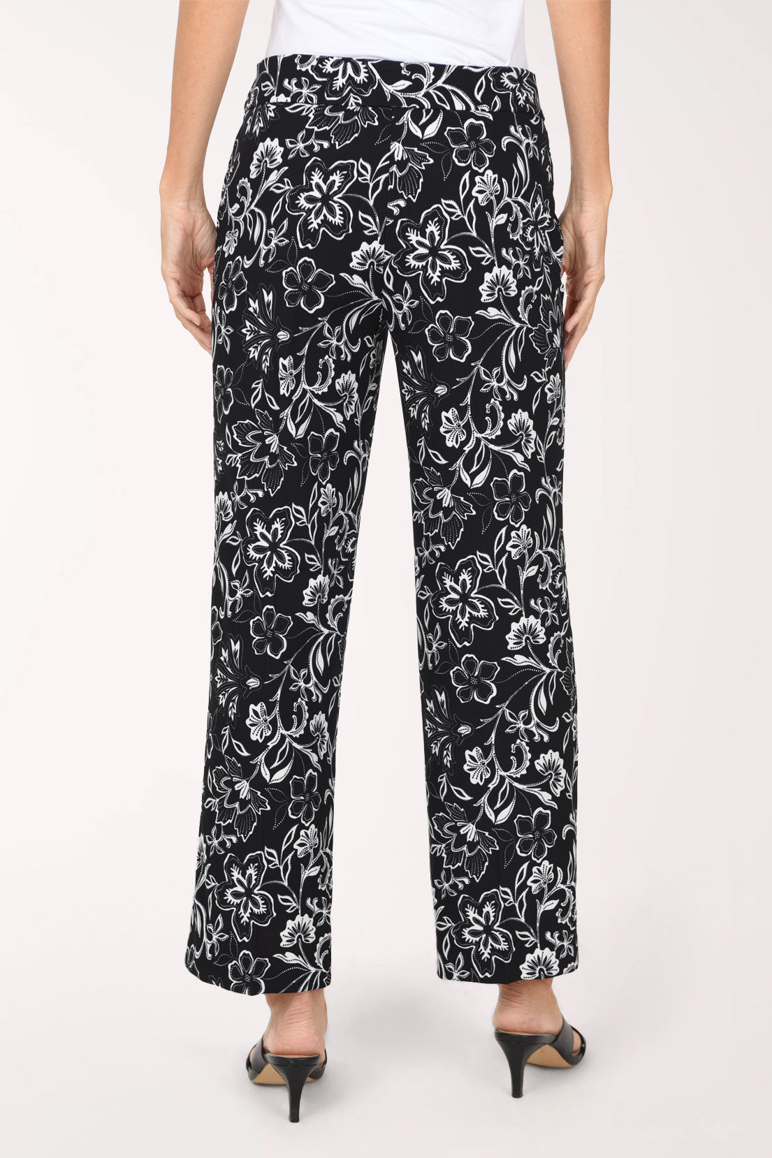 A person wearing black wide-leg cropped pants with a white floral print, paired with a white top and black slide sandals, shown against a plain light background.