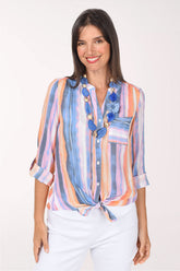 Model wearing the Zac and Rachel Autumn Sunset Striped Button-Front Blouse, watercolor stripes in periwinkle, navy, lavender and peach, tied at the front over white pants