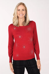 Model wearing the Zac and Rachel Crystal Sparkle Crewneck Sweater, a red knit sweater with clear crystal starbursts across the front, over black plaid pants, front view