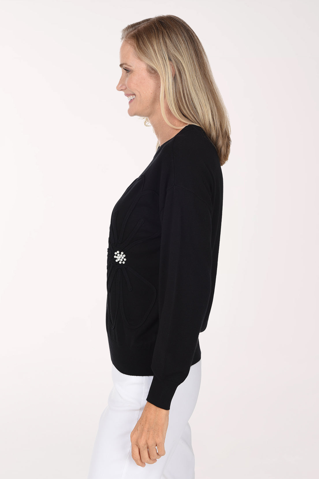 Woman wearing a sold black sweater with a pearl button accent on waist