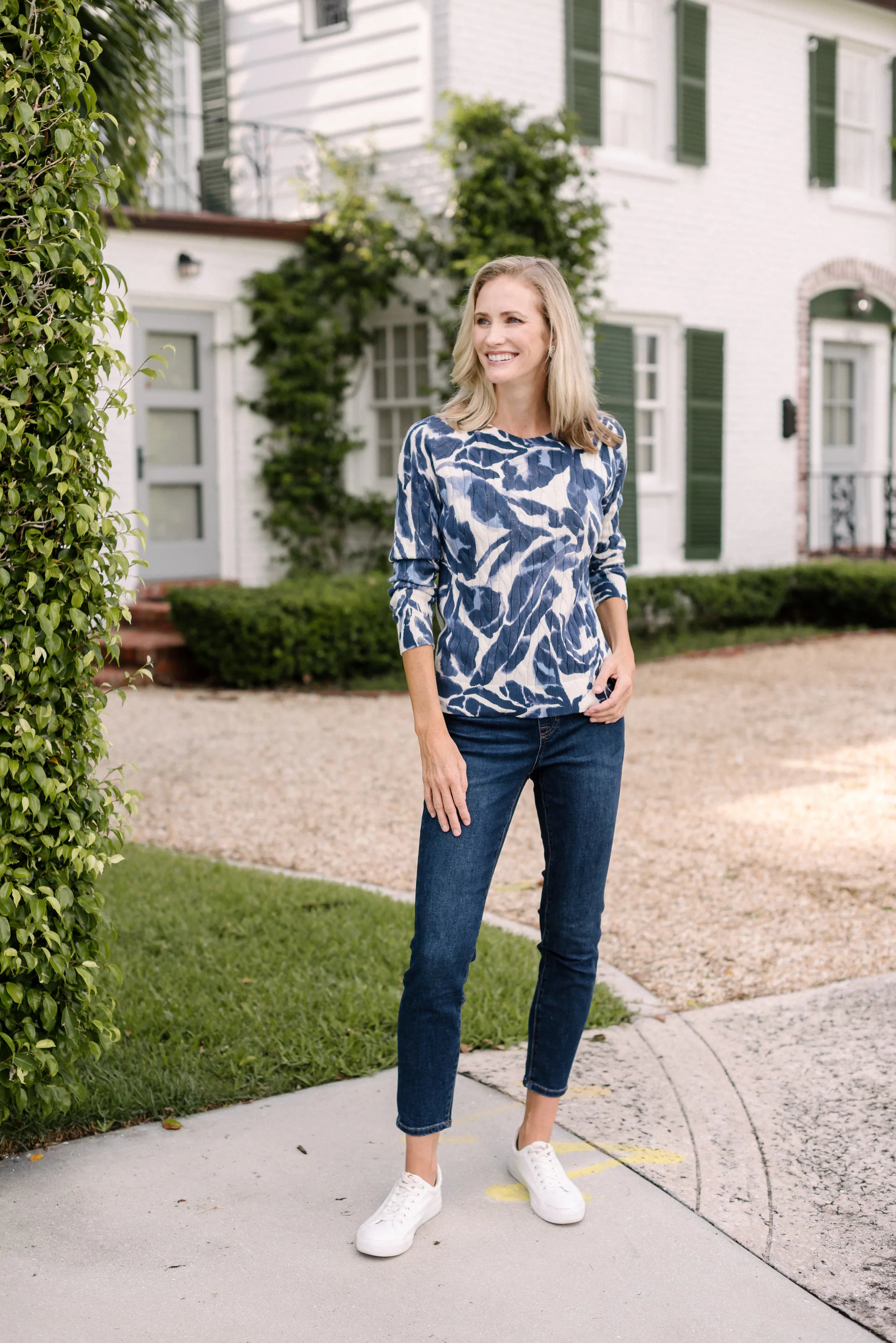 Full-length view of a woman in a navy-and-white botanical top and dark jeans.
