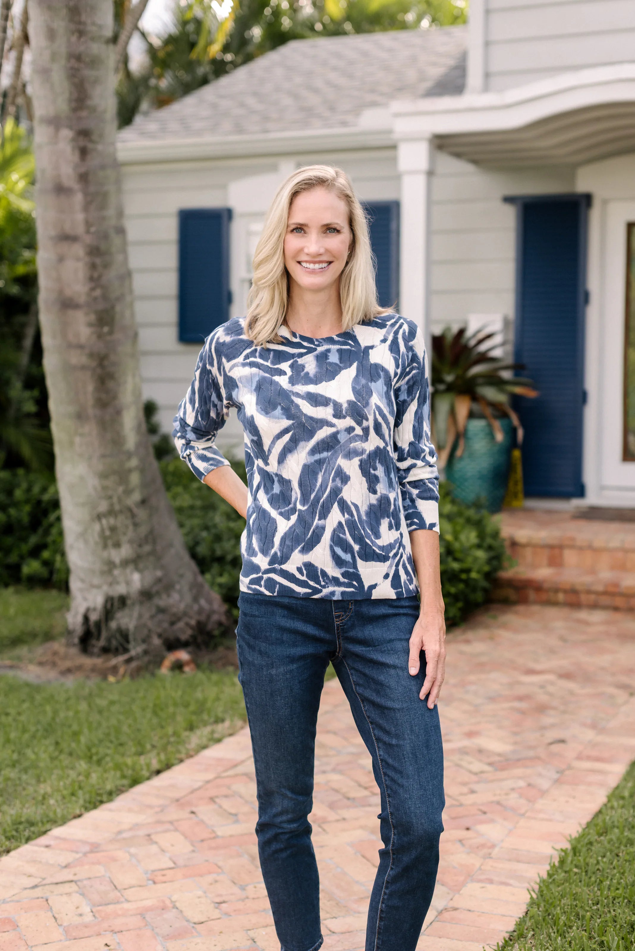 Woman in a navy-and-white botanical top framed by colorful flowers.