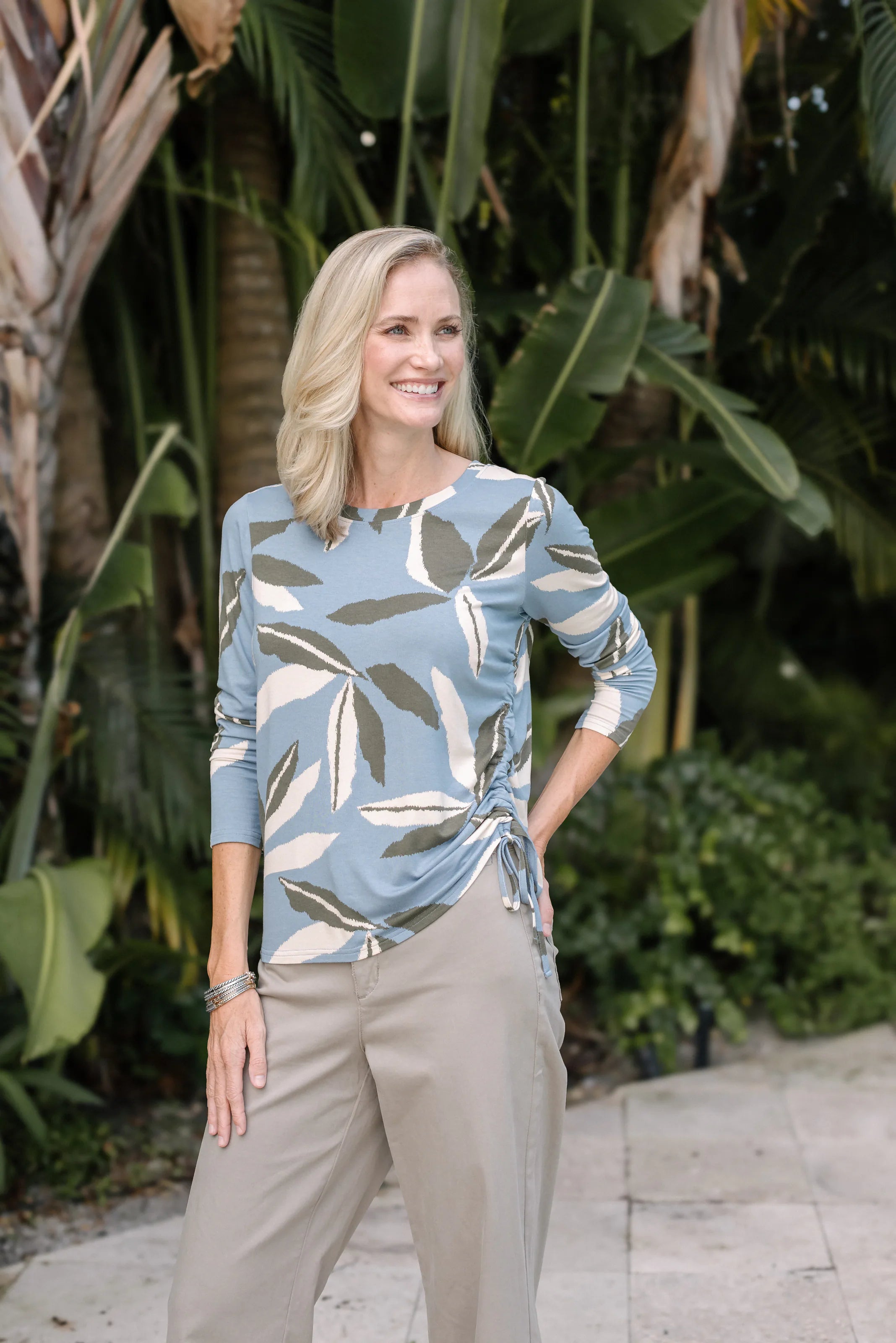 Woman wearing a blue-green leaf-print blouse with light neutral pants.