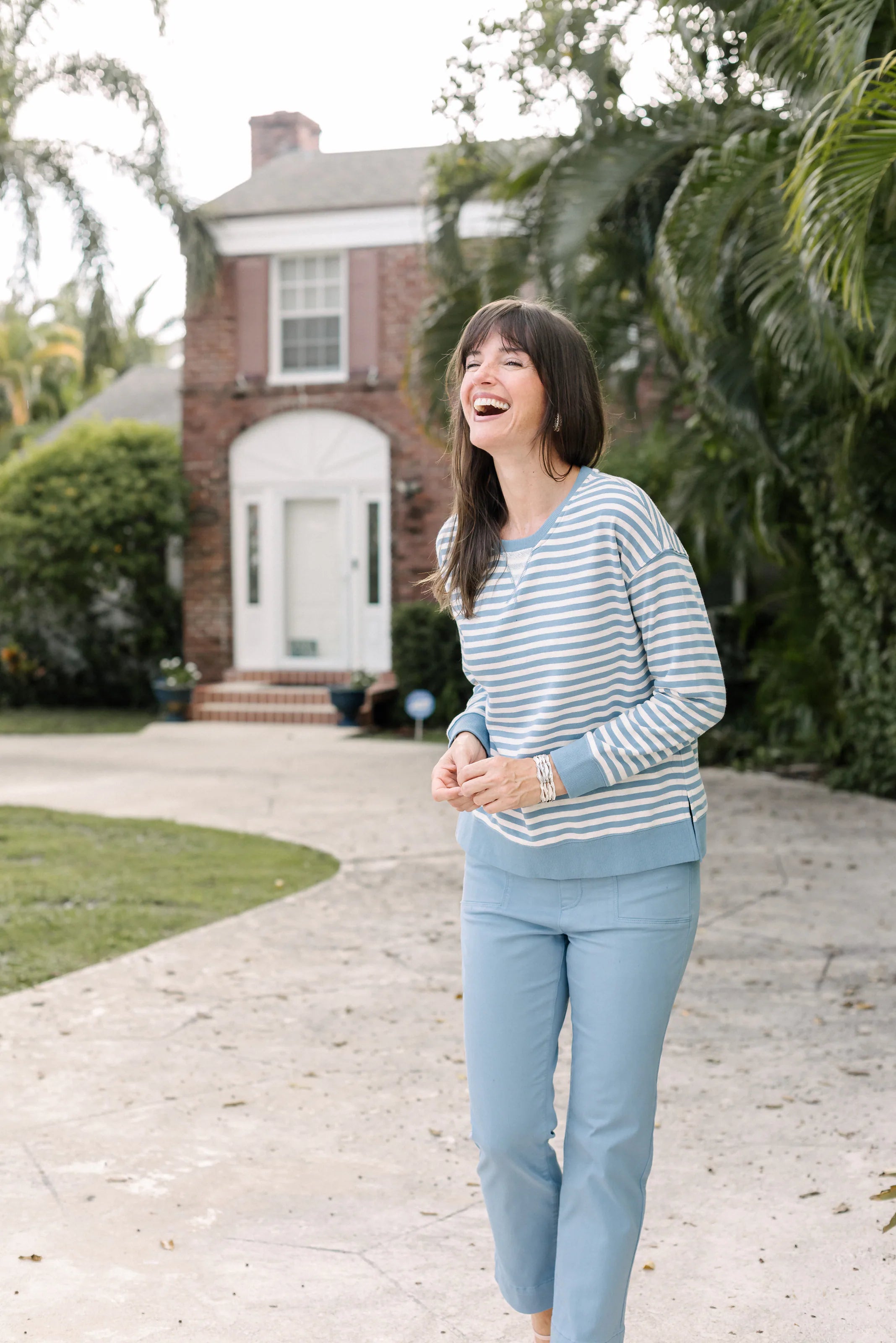 Woman in a blue-and-white striped top outside a white coastal house.