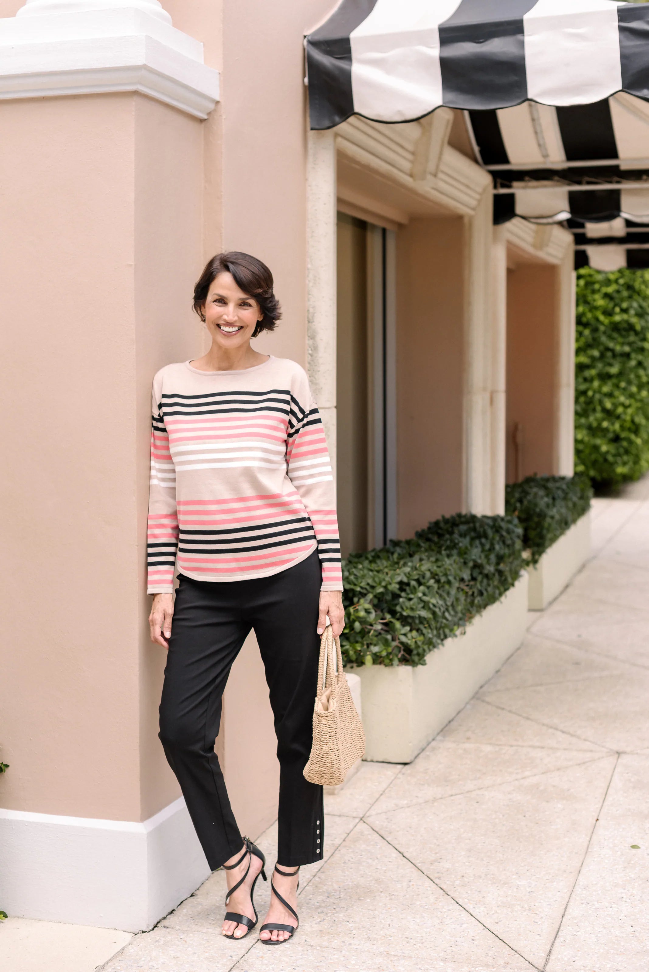 Woman wearing a pink, black and white striped top with black pants.
