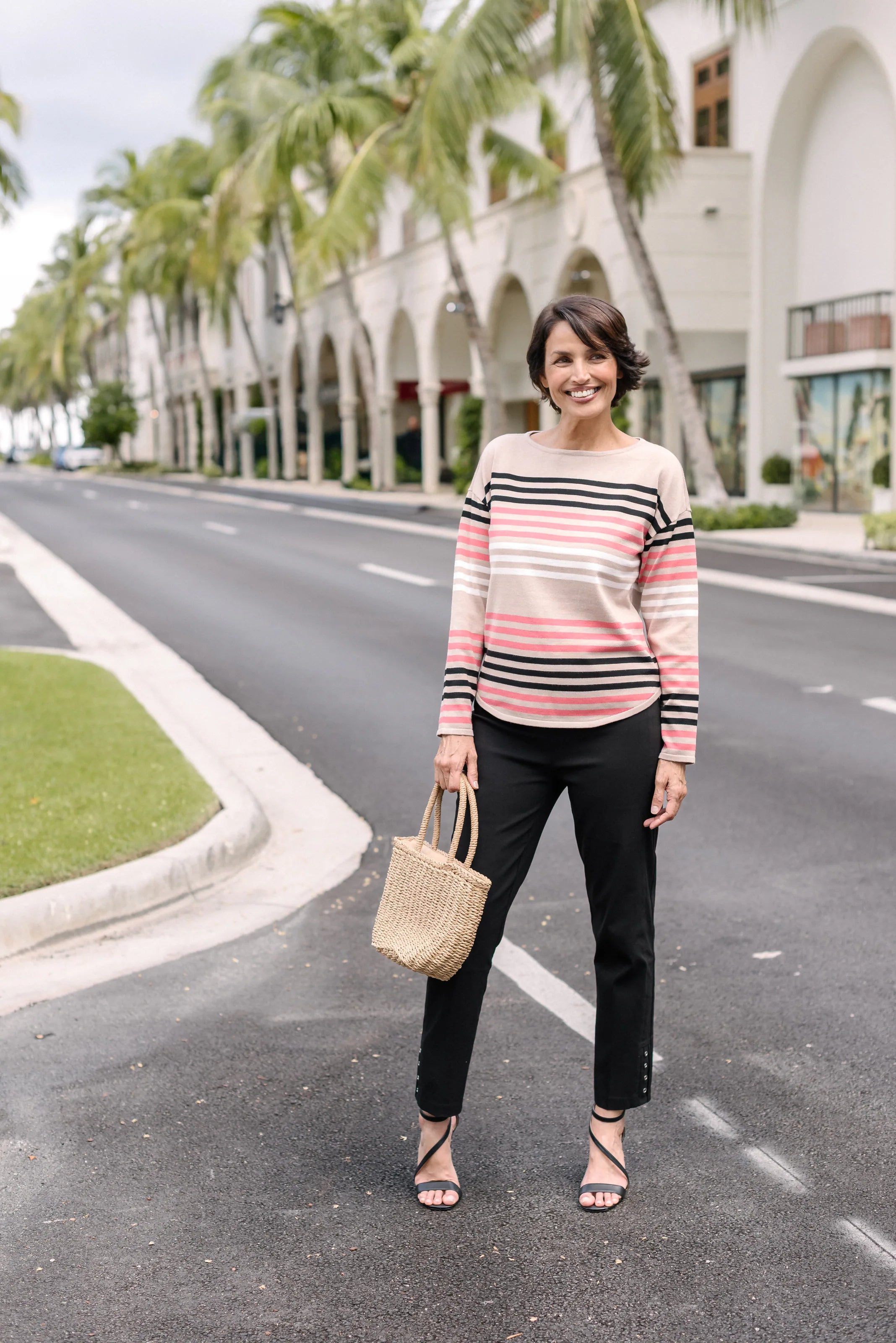 Full-length view of a woman in a striped top and black pants holding a handbag.