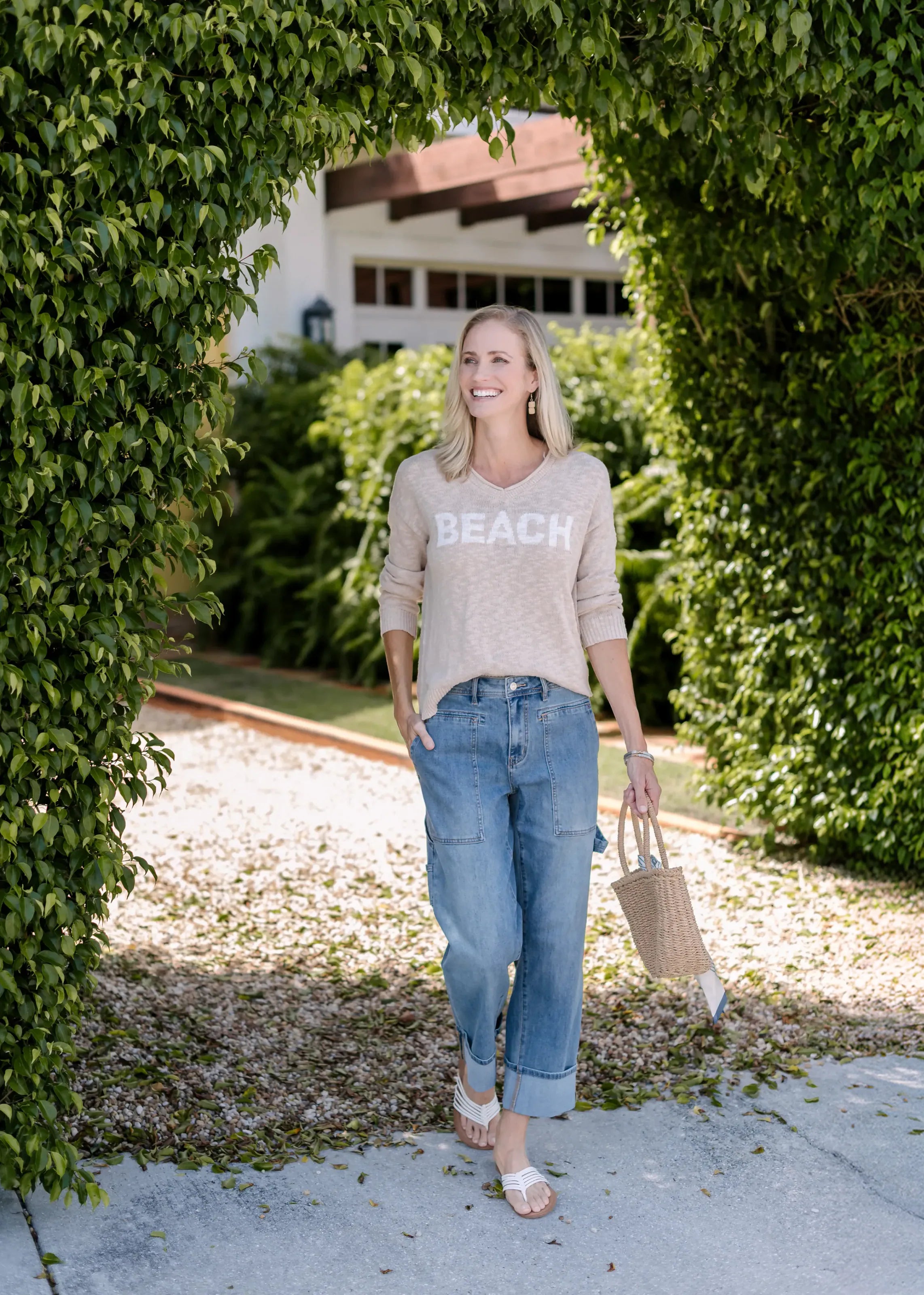 Full-length view of a woman wearing a taupe BEACH sweater and jeans.