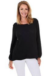 A woman wearing a long sleeve black cotton scoop neck sweater, with a seam down the front and white pants.