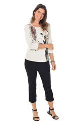 A full length shot of a model wearing black pull-on capri pants with an elastic waistband and side slits at the hemline, paired with a white top and black sandals.